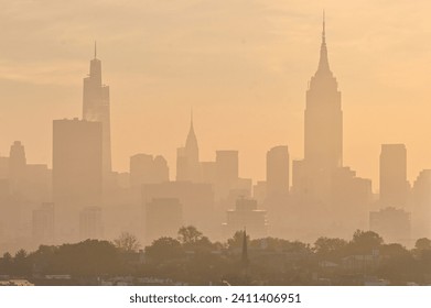 Horizontal photo of silhouetted midtown New York City skyline in a yellow haze with Hoboken in the foreground  - Powered by Shutterstock