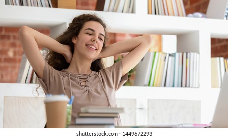 Horizontal Photo Smiling Teenage Girl Student Relaxing During Break In Library, Sitting In Comfortable Chair, Holding Hands Behind Head, Woman Finished Work With Books And Laptop, Enjoying Free Time