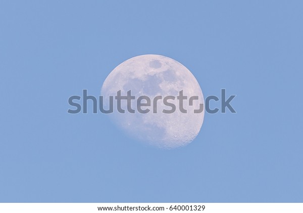Horizontal photo of white big\
moon. Moon is captured during a day time with clear blue sky and\
few days before full-moon so only small part is hidden in shadow of\
Earth.