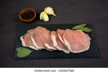 Horizontal Photo Of Whole Pork Tenderloin Raw Meat Is On A Black Slate Dish With  Pepper Salt Aromatic Herbs And White Garlic