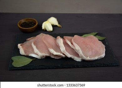 Horizontal Photo Of Whole Pork Tenderloin Raw Meat Is On A Black Slate Dish With  Pepper Salt Aromatic Herbs And White Garlic