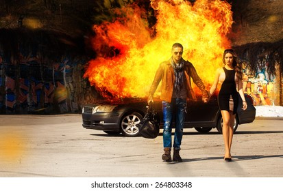 Horizontal picture of the blockbuster as a man and a woman go away from burning car outdoors