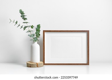 Horizontal picture frame mockup in white minimalistic scandinavian interior with fresh eucalyptus decorations. Blank mockup for artwork, print or photo presentation. - Shutterstock ID 2253397749