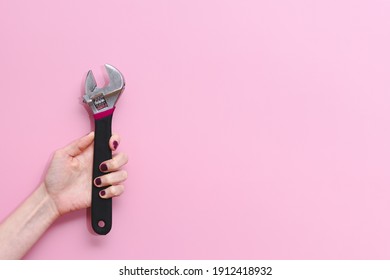 horizontal picture of the hand of a caucasian young woman holding an adjustable monkey wrench tool on a pink background. Concept of equality at work and woman strength. Copy space on the right