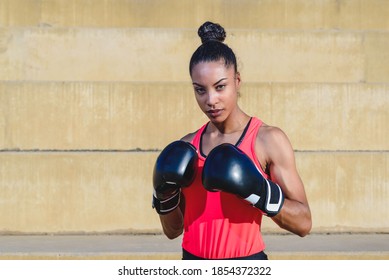 horizontal portrait of an attractive african woman wearing sport clothes and boxing gloves standing in defense pose - Powered by Shutterstock