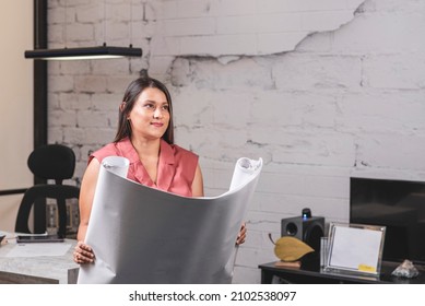 Horizontal Portrait Of A Beautiful Latina Woman Holding Construction Plans In Her Hands In An Office. 
