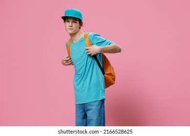 Horizontal Portrait In A Blue T-shirt And Cap With An Orange Backpack On His Back, Standing Sideways To The Camera. Studio Photo On A Plain Pink Background With Space For An Advertising Mockup