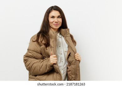 Horizontal Portrait Of An Brunette Woman Against A Light Background Standing In A Warm Winter, Stylish Jacket And Holding Her Edges With Her Hands. Studio Photography With Empty Space On Background