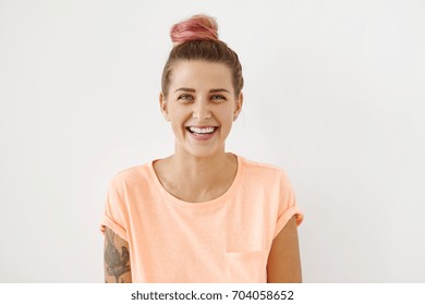 Horizontal Portrait Of Cheerful Woman With Appealing Smile, Having Pinkish Hair Bun And Tattoo, Wearing Casual Clothes, Isolated Over White Background. Beautiful Female Showing Her Pleasant Emotions