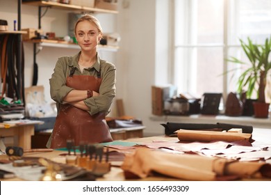 Horizontal Portrait Of Confident Caucasian Woman Wearing Apron Standing With Arms Crossed In Modern Leather Craft Workshop Looking At Camera, Copy Space