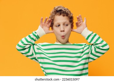 horizontal portrait of a cute, funny, playful, curly-haired boy of school age in a striped long-sleeved t-shirt on an orange background, emotionally grimacing