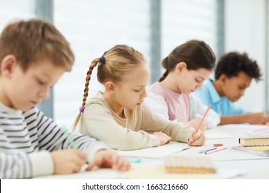 Horizontal portrait of four children wearing casual outfits sitting at desk in modern classroom writing something in their notebooks, copy space - Shutterstock ID 1663216660