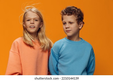 Horizontal Portrait Of A Happy Brother And Sisters On An Orange Background Smiling Cutely. Studio Photo With Empty Space For Advertising Mockup