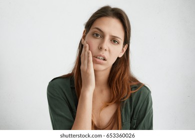 Horizontal portrait of pretty sad woman with bright dark eyes and straight hair holding hand on cheek looking upset after hard work. Exhausted female student after session having sad expression - Shutterstock ID 653360026