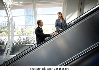 Horizontal profile shot of a businessman and businesswoman smiling at each other on an escalator going up in a building. - Powered by Shutterstock