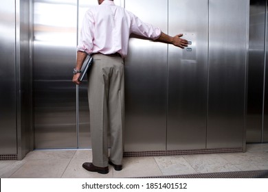 Horizontal rear view of lower section of a businessman holding a laptop pressing button to call lift with copy space.