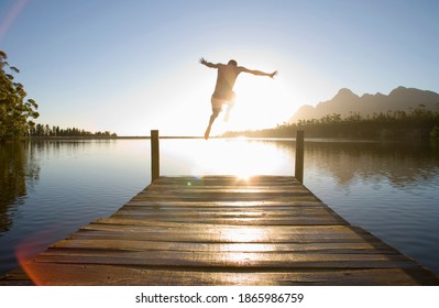 Horizontal rear view of a man leaping from a jetty into the lake at sunset. - Powered by Shutterstock