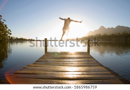 Horizontal rear view of a man leaping from a jetty into the lake at sunset.