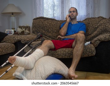 Horizontal shot of an adult man with his leg in a cast and bandaged on a stool with crutches at his side talking on the mobil. Concept of rehabilitation after serious physical accident injury