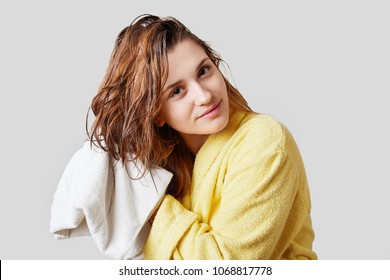 Horizontal Shot Of Attractive Female Wipes Wet Hair With Towel, Wears Yellow Bathrobe, Has Pleased Expression, Going To Make Hairstyle, Prepares For Special Occasion, Wants Look Beautifully.