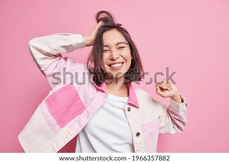 Foto Bild Frau mit dunkler Jacke und kurzen Jeans steht barfuß auf einem Bein vor hellgrüner Wand und hält einen Regenschirm hoch