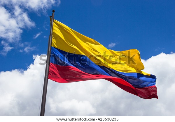 Horizontal shot of the colombian
flag being move by the wind over sky and clouds on a sunny
day.