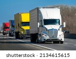 Horizontal shot of a color convoy of heavy semi trucks on the highway.