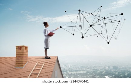 Horizontal Shot Of Confident Woman Doctor In White Medical Suit Standing At The Top Of Brick Building And Interracting With Network Structure. Modern Medical Industry Concept