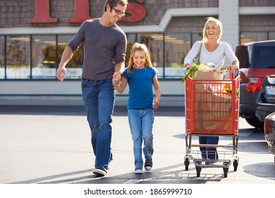 Horizontal Shot Of A Couple With Their Daughter Exiting From A Super Market With The Woman Pushing The Shopping Cart.