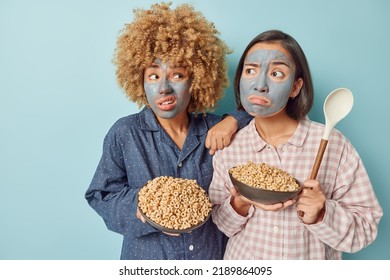 Horizontal Shot Of Diverse Women Stand Closely To Each Other Awake Early Morning Eat Healthy Breakfast Dressed In Slumber Suit Undergo Beauty Skin Care Procedures Isolated Over Blue Background