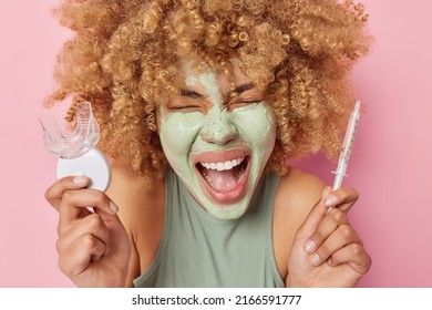 Horizontal Shot Of Emotional Woman Screams Emotionally Applies Nourishing Clay Mask On Face Holds Plastic Mouth Expander And Syringe With Liquid Undergoes Daily Beauty Procedures Stands Indoor