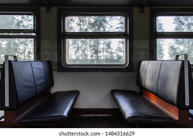 Horizontal Shot Of Empty Seats Facing Each Other Inside Passenger Car Of Old Suburban Electric Multiple Unit, And Window Between Seats With Natural Landscape Blurred While Train Motion