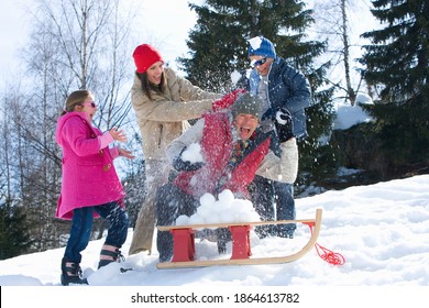 Horizontal Shot Of A Family Of Four Having A Snow Ball Fight In A Snow Covered Field With A Sled In The Foreground On A Bright, Sunny Day