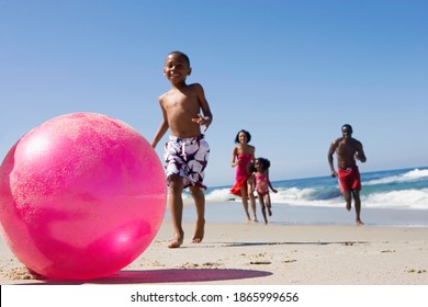 Horizontal shot of a family of four playing with a pink ball on the beach with selective focus on the ball. - Powered by Shutterstock