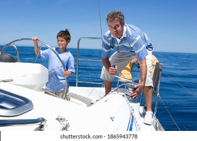 Horizontal shot of father and son standing on the deck of sailing boat on a sunny day.