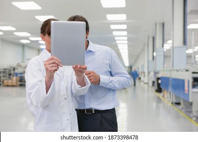 Horizontal Shot Of A Female Scientist And A Businessman Looking At A Digital Tablet With Obscured Faces On A Factory Floor With Copy Space.