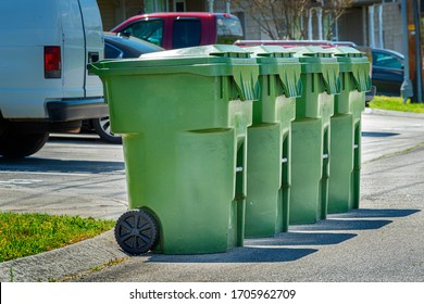 Horizontal Shot Of Four Residential Garbage Containers Lined Up On The Street For Pickup.