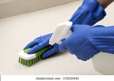 Horizontal Shot Of Hands Wearing Rubber Gloves And Cleaning Counter With Brush And Spray Cleaner/ Scrubbing Wearing Rubber Gloves/ Focus Is On The Spray Bottle 