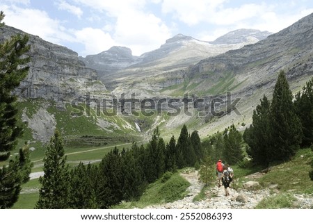 Horizontal shot of hikers walking down a mountain trail in Ordesa and Monte Perdido National Park in the Aragonese Pyrenees of Northern Spain. The Cola de Caballo waterfall is seen in the background.