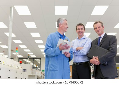 Horizontal Shot Of An Joyous Engineer With A Clipboard Besides An Investor And A Manager On The Factory Floor Smiling At The Camera.