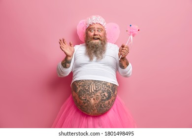 Horizontal Shot Of Joyous Funny Man With Thick Beard And Big Fat Belly, Plays Fairy On Costume Party, Chills During Spare Time, Sends Positive Vibes, Works As Animator, Isolated Over Rosy Background