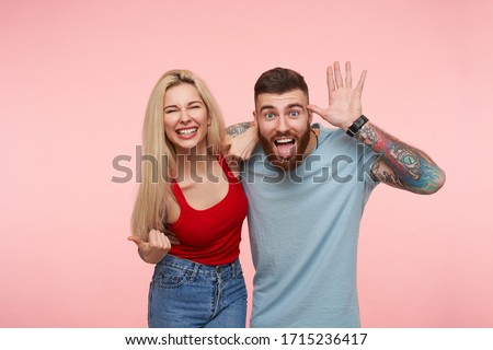 Horizontal shot of lovely joyful pair of young people fooling and laughing while spending nice time togehter, isolated over pink background in casual wear