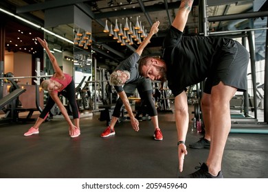 Horizontal shot of mature woman and man learning to perform body friendly warm up routines before main workout in gym. Professional trainer showing right patterns of movements. Aged people in sport.