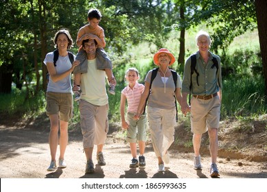 Horizontal shot of a multi-generational family with boy on the father's shoulder hiking on a mountain trail smile at the camera.