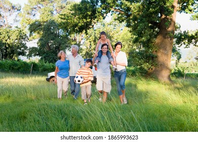 Horizontal shot of a multi-generational family walking in a woodland clearing with boy holding a soccer ball and his sister on dad's shoulder. - Powered by Shutterstock