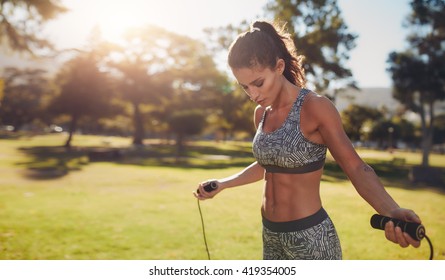 Horizontal Shot Of Muscular Woman With Skipping Rope Outdoors In Nature. Fitness Female Doing Skipping Workout With Jump Rope In A Park On A Sunny Day.