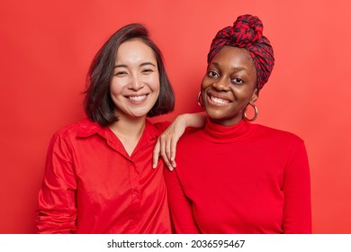 Horizontal shot of optimistic mixed race young women pose for making common photo smile happily being in good mood spend free time together dressed casually isolated over vivid red background - Powered by Shutterstock