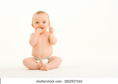 Horizontal Shot Of A Seated Baby Boy In Diaper Pants Sucking Fingers Looks At The Camera With Copy Space.