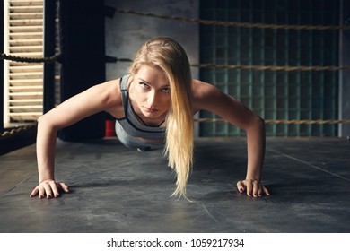 Horizontal shot of self determined gorgeous young sportswoman with loose dyed hair doing push ups planting hands widely on floor inside boxing ring, looking at camera with serious facile expression - Powered by Shutterstock