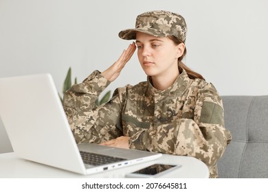 Horizontal shot of serious female soldier wearing military costume, poising indoor in light room, having online conversation and saluting to camera, saying yes sir. - Shutterstock ID 2076645811
